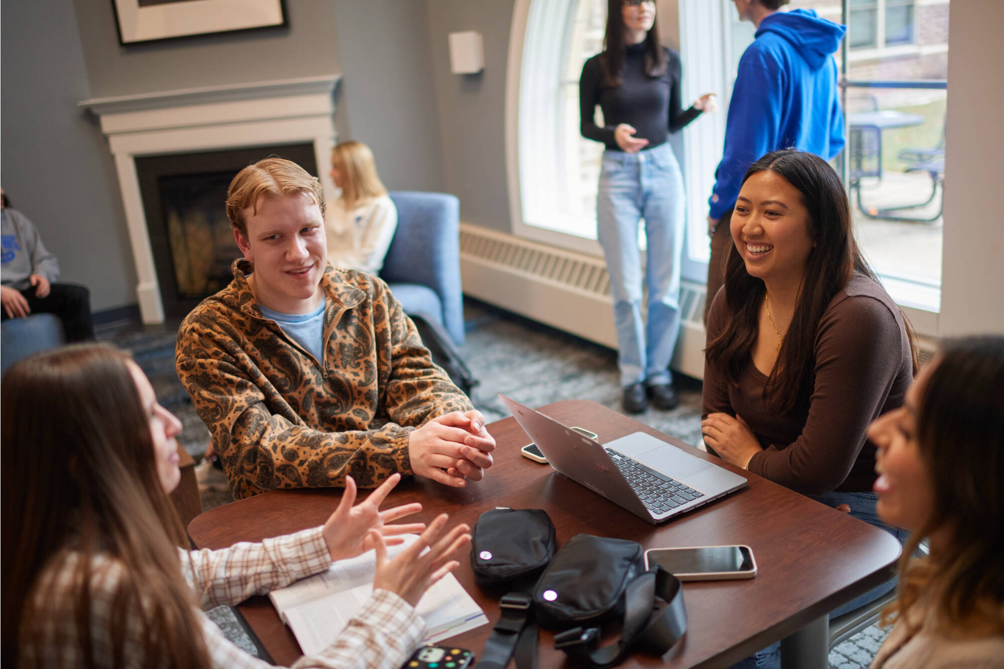Students talk happily around a table in a community area in a living center.